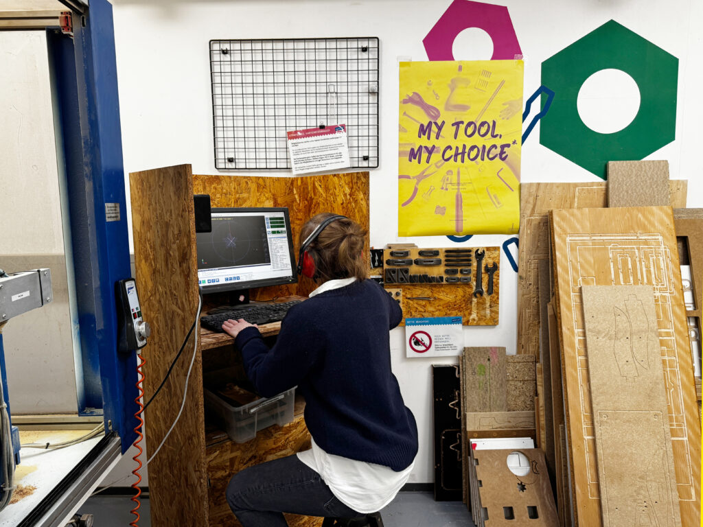 “My tool, my choice” poster in a makerspace workshop behind a woman operating a CNC milling machine.